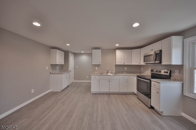 kitchen featuring white cabinets, appliances with stainless steel finishes, light stone countertops, light hardwood / wood-style flooring, and sink