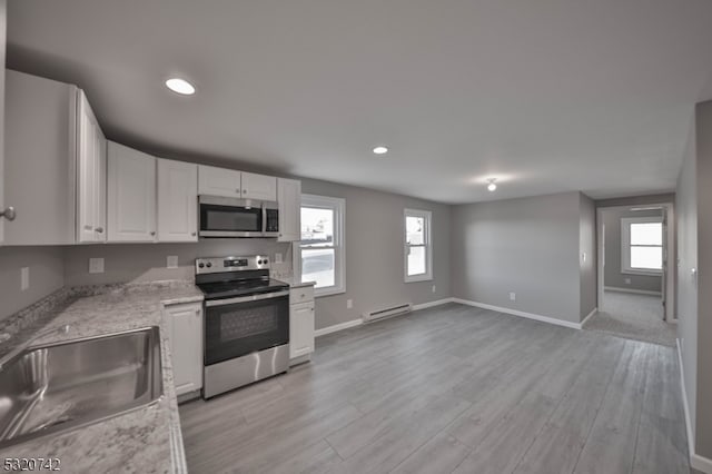 kitchen with appliances with stainless steel finishes, a baseboard radiator, plenty of natural light, and white cabinets