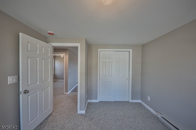 unfurnished bedroom with a closet, light carpet, and a baseboard heating unit