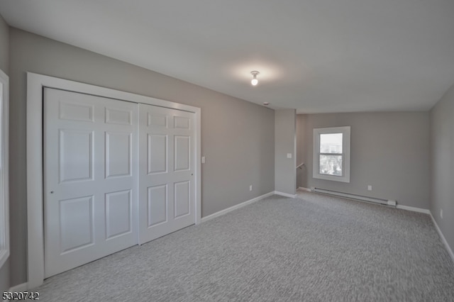 unfurnished bedroom with a closet, a baseboard heating unit, and light colored carpet