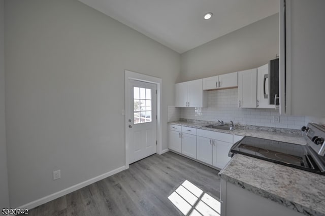 kitchen featuring stainless steel electric stove, sink, white cabinetry, light hardwood / wood-style floors, and tasteful backsplash