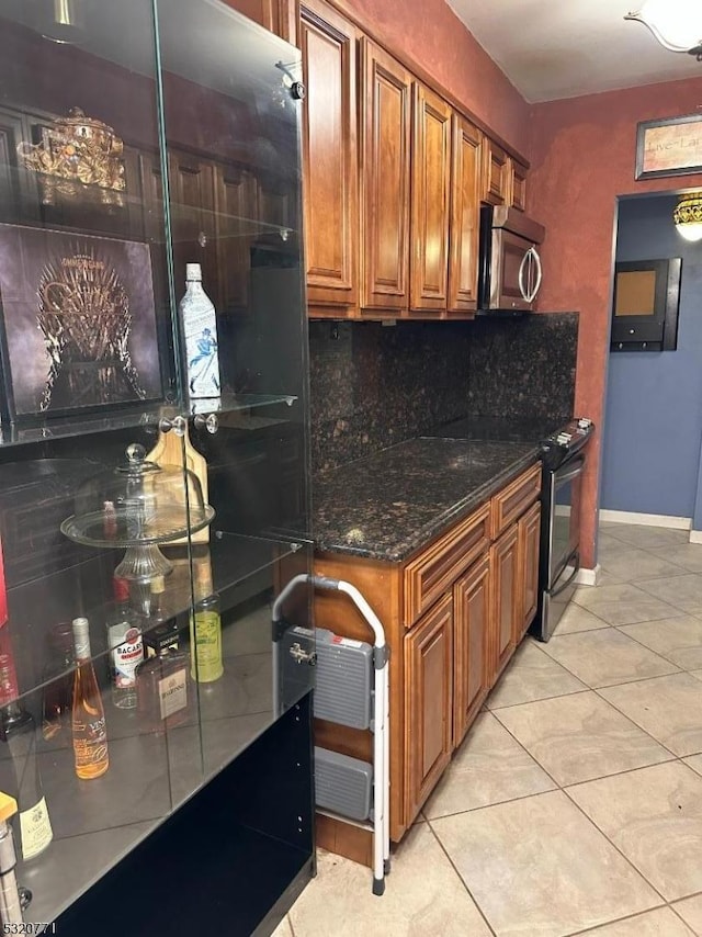 kitchen featuring light tile patterned floors, backsplash, black range with electric cooktop, and dark stone counters