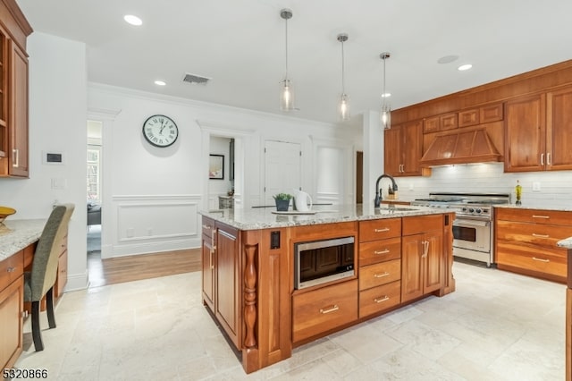 kitchen with premium range hood, a kitchen island with sink, stainless steel appliances, sink, and decorative light fixtures