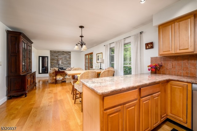 kitchen with light stone countertops, a notable chandelier, light wood-type flooring, and kitchen peninsula