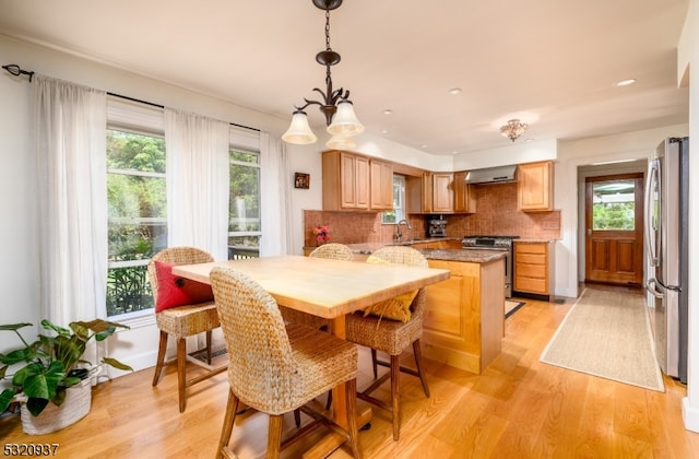 kitchen with light wood-type flooring, stainless steel appliances, tasteful backsplash, and wall chimney range hood