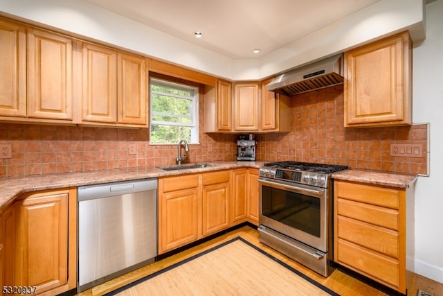 kitchen with wall chimney exhaust hood, sink, light stone countertops, and stainless steel appliances