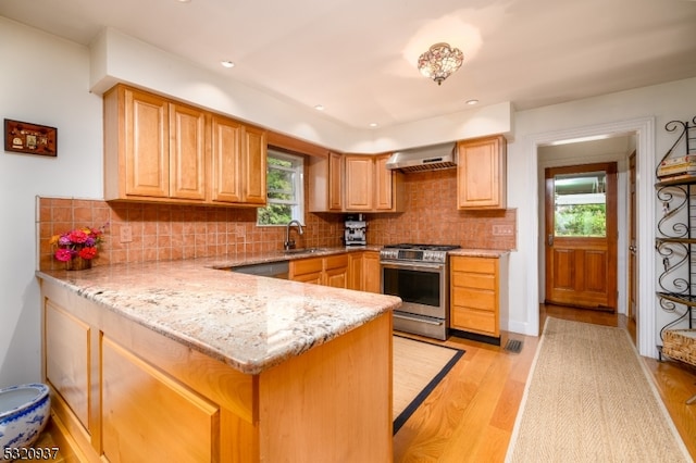 kitchen with light stone countertops, light wood-type flooring, gas stove, wall chimney range hood, and sink