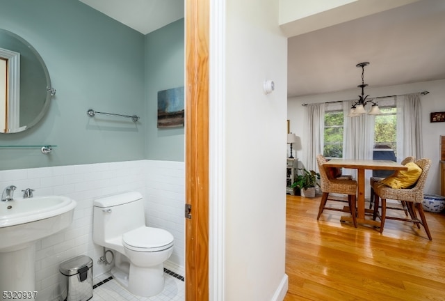 bathroom with toilet, wood-type flooring, tile walls, and a notable chandelier