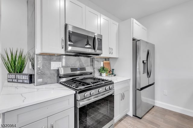 kitchen featuring decorative backsplash, light hardwood / wood-style flooring, light stone countertops, white cabinetry, and appliances with stainless steel finishes