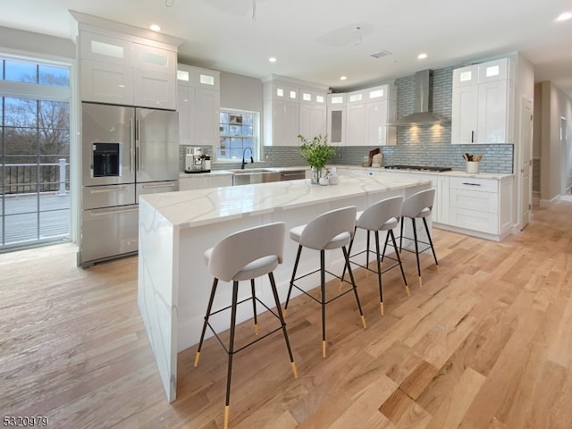 kitchen with wall chimney exhaust hood, white cabinets, a center island, and stainless steel fridge with ice dispenser