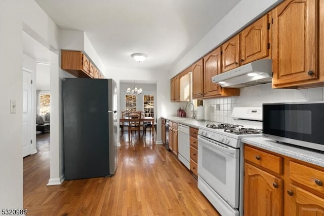 kitchen with sink, an inviting chandelier, stainless steel appliances, light hardwood / wood-style floors, and backsplash