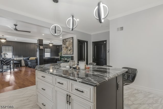 kitchen featuring light hardwood / wood-style floors, dark stone counters, hanging light fixtures, a kitchen island, and white cabinetry