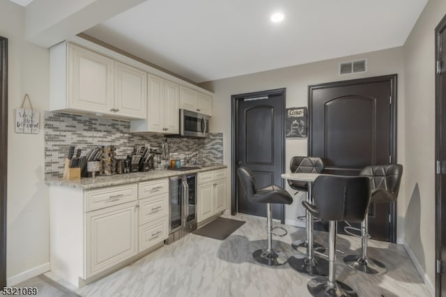 kitchen with light stone countertops, wine cooler, and tasteful backsplash