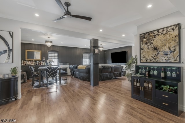 living room with hardwood / wood-style floors, ceiling fan with notable chandelier, wooden walls, and crown molding