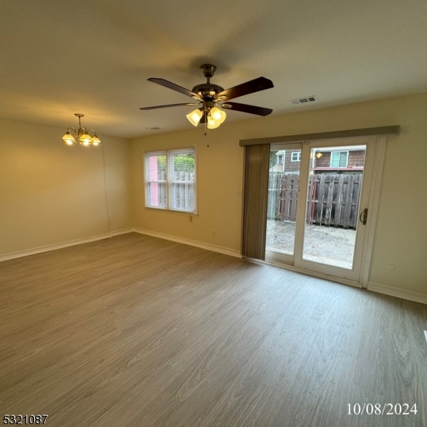 spare room featuring wood-type flooring and ceiling fan with notable chandelier