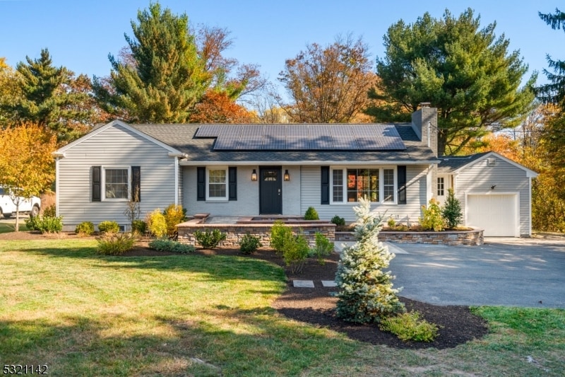 ranch-style home featuring a garage, solar panels, and a front lawn