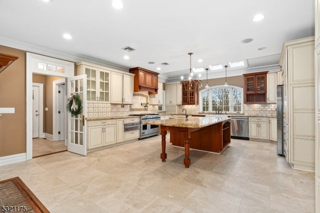 kitchen with a kitchen breakfast bar, cream cabinets, an island with sink, and appliances with stainless steel finishes