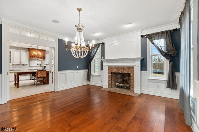 unfurnished living room with a fireplace, ornamental molding, a notable chandelier, and light wood-type flooring