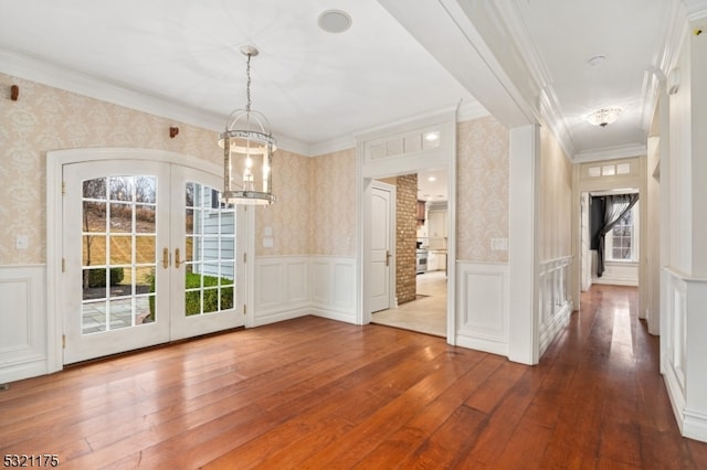 unfurnished dining area featuring french doors, hardwood / wood-style flooring, ornamental molding, and a notable chandelier