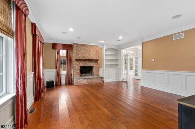 unfurnished living room featuring built in shelves, dark wood-type flooring, ornamental molding, and a healthy amount of sunlight