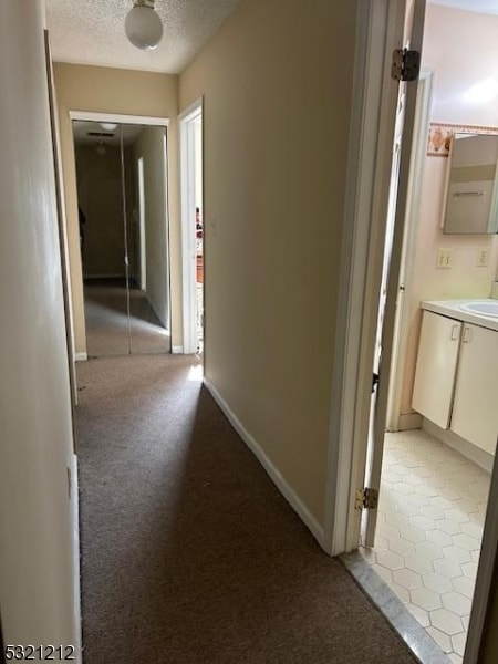 hallway featuring a textured ceiling, light colored carpet, and sink