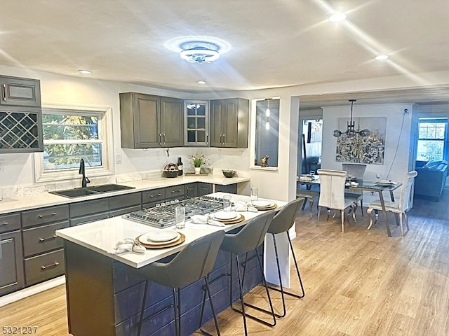 kitchen with hanging light fixtures, stainless steel gas stovetop, light wood-type flooring, a center island, and sink