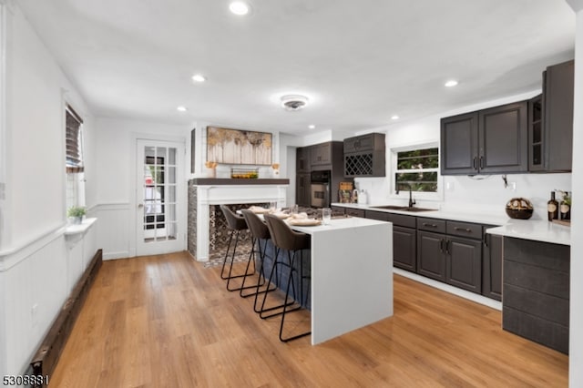 kitchen with a kitchen island, light hardwood / wood-style flooring, black oven, sink, and a kitchen bar