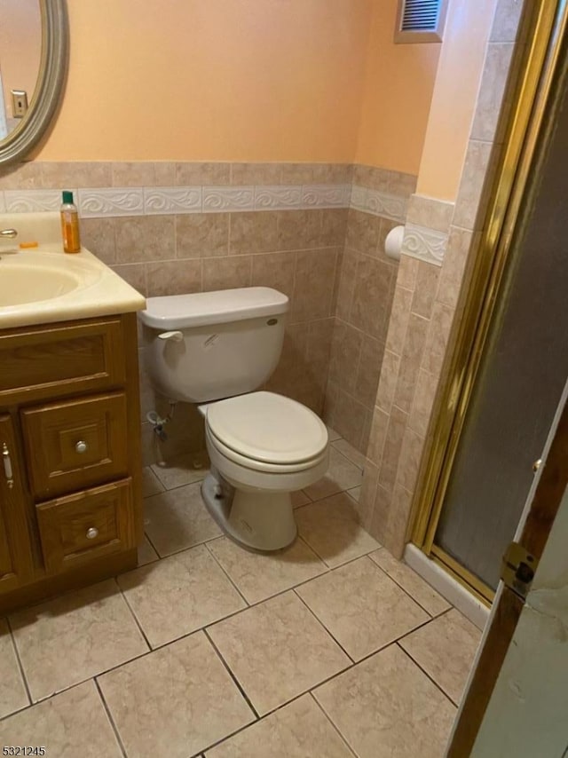 bathroom with vanity, a shower with door, tile patterned flooring, toilet, and tile walls