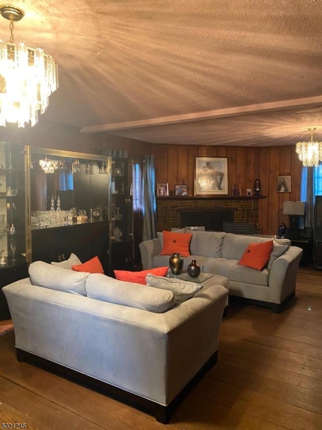 living room featuring a stone fireplace, wood walls, hardwood / wood-style floors, a chandelier, and a textured ceiling