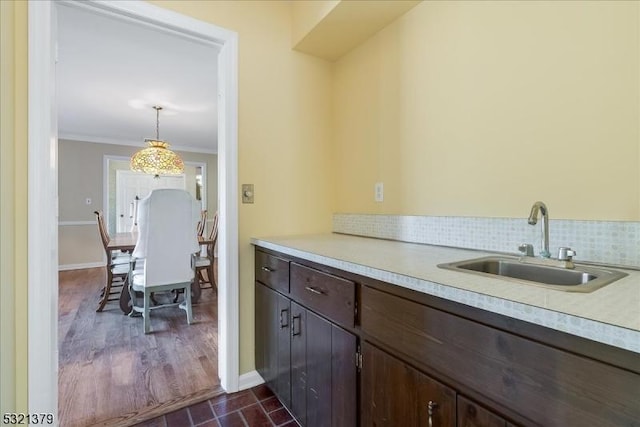 kitchen with pendant lighting, dark hardwood / wood-style flooring, sink, crown molding, and dark brown cabinets