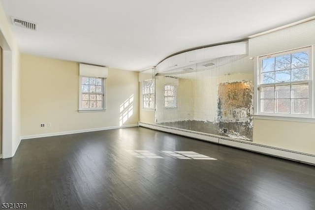 spare room featuring a baseboard heating unit, dark hardwood / wood-style flooring, and a wealth of natural light