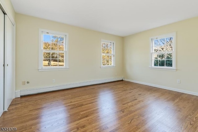 unfurnished bedroom with baseboard heating, a closet, and hardwood / wood-style floors