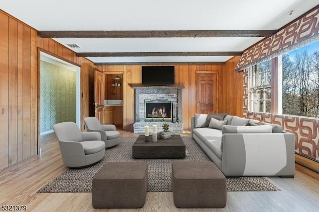 living room featuring light hardwood / wood-style flooring, a fireplace, beam ceiling, and wood walls