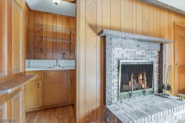 room details with a brick fireplace, sink, wood-type flooring, and wooden walls