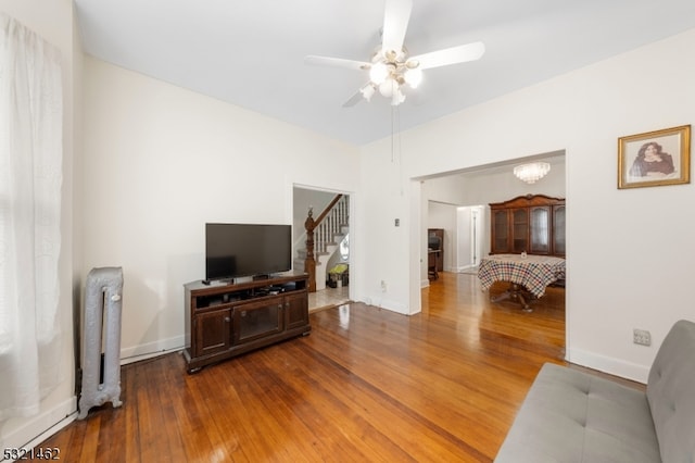 living room with radiator heating unit, wood-type flooring, and ceiling fan with notable chandelier