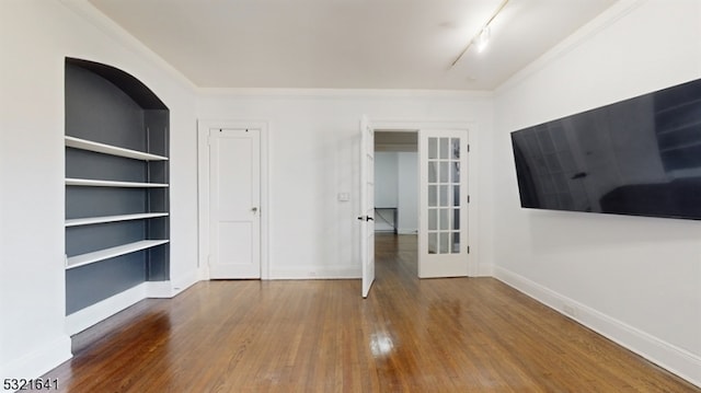 empty room with french doors, track lighting, built in shelves, crown molding, and wood-type flooring