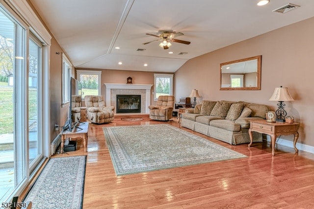 living room with ceiling fan, light hardwood / wood-style flooring, vaulted ceiling, and a tiled fireplace