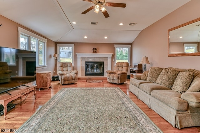 living room featuring vaulted ceiling, a tile fireplace, ceiling fan, and light hardwood / wood-style flooring