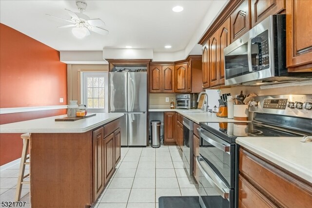 kitchen featuring a breakfast bar, ceiling fan, stainless steel appliances, and light tile patterned floors