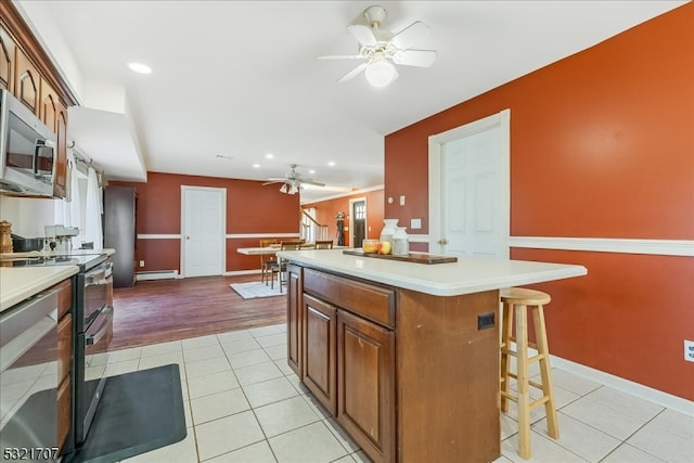 kitchen with appliances with stainless steel finishes, a center island, light hardwood / wood-style floors, baseboard heating, and a breakfast bar