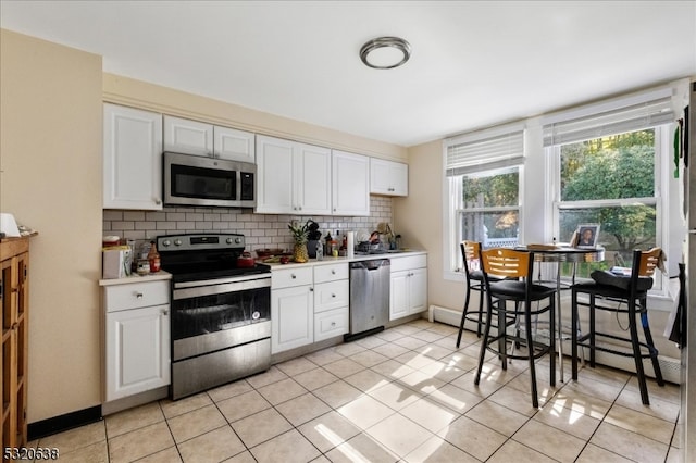 kitchen with white cabinets, light tile patterned floors, appliances with stainless steel finishes, backsplash, and baseboard heating