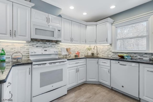 kitchen featuring light wood finished floors, decorative backsplash, white cabinets, a sink, and white appliances