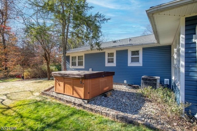 rear view of house featuring a hot tub, roof with shingles, central AC, and a yard