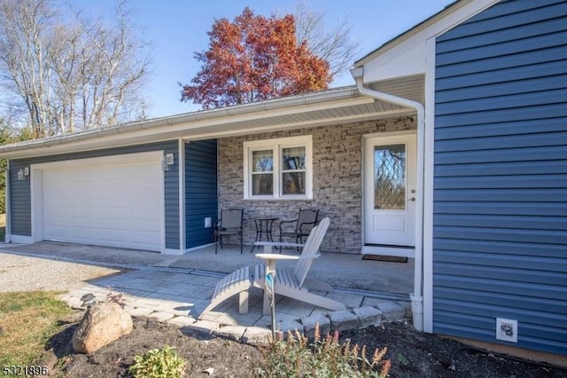 entrance to property featuring a garage, stone siding, and covered porch