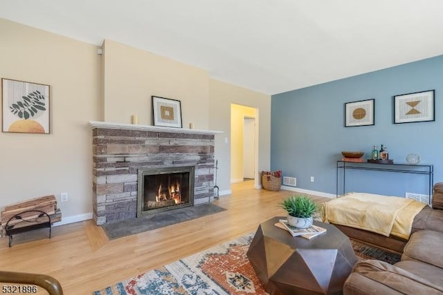 living area with visible vents, baseboards, wood finished floors, and a stone fireplace