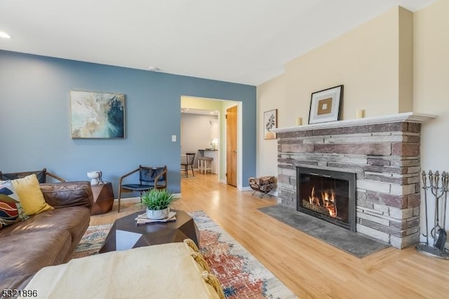 living room featuring a stone fireplace, baseboards, and wood finished floors