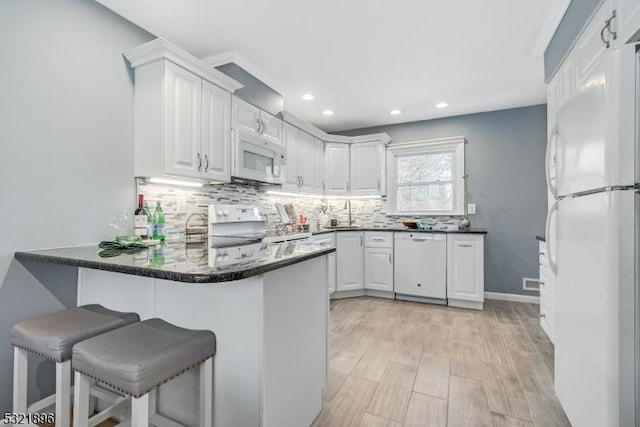 kitchen with a peninsula, white appliances, backsplash, and white cabinets