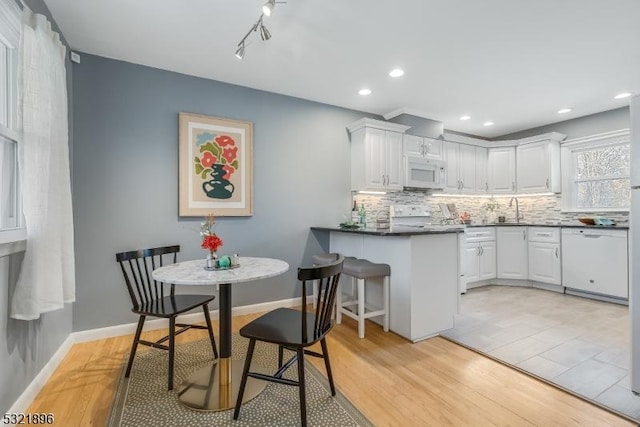 kitchen featuring a peninsula, white appliances, a sink, white cabinetry, and decorative backsplash