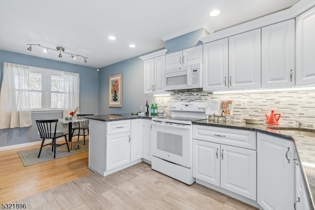 kitchen with a peninsula, white appliances, white cabinetry, and decorative backsplash