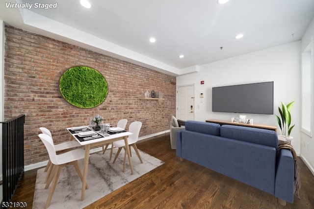 living room featuring dark wood-type flooring and brick wall